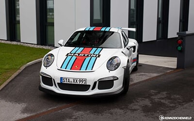 Weißer Porsche mit "Martini" Folierung auf einer Auffahrt