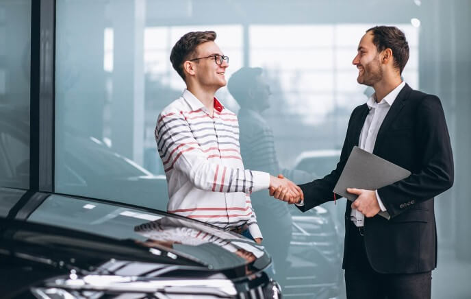 Zwei Männer geben sich die HAnd neben einem verkauften Auto